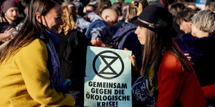 Zwei Demonstrantinnen halten ein Plakat und blicken sich gegenseitig in die Augen