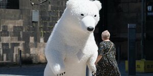 Ein lebensgroßes Eisbärenstofftier steht vor einem Gebäude, eine Frau läuft daran vorbei