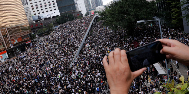 Eine große Demonstration auf einer Straße wird mit einem Handy gefilmt
