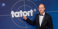 Tatort-Schauspieler Martin Brambach zeigt auf das Logo der Sendung