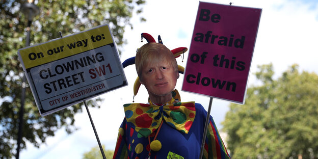 Eine Person im Clowns-Kostüm mit einer Maske von Boris Johnson