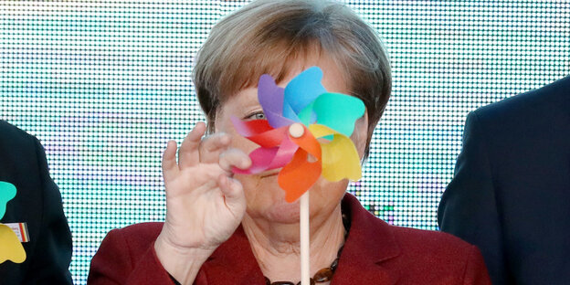 Angela Merkel, vor ihrem Gesicht ein Spielzeug-Windrad