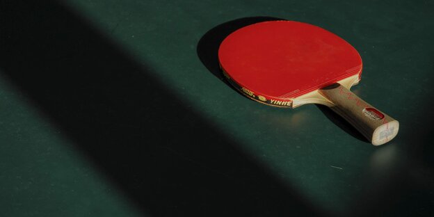Eine rote Tischtennis-Kelle liegt auf einer grünen Tischtennis-Plattte