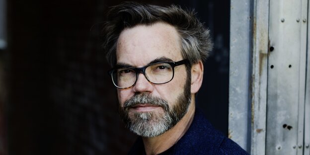 Zu sehen ist das Gesicht des Autors David Wagner, mit grau-schwarzem Haar und Bart und einer schwarz umrandeter Brille
