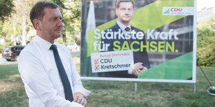 Michael Kretschmer ist von der Seite zu sehen. Er krempelt sich die Hemdärmel hoch. Im Hintergrund ist ein großes Wahlplakat, auf dem er abgebildet ist