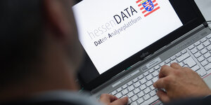 Ein Kriminalbeamter sitzt im Frankfurter Polizeipräsidium vor einem Laptop, auf dessen Bildschirm die Aufschrift "hessenDATA Daten-Analyseplattform" zu lesen ist.