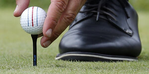 Ein Mann legt einen Golfball auf den Abschlagsstift, man sieht seine Hand und einen Teil des Schuhs