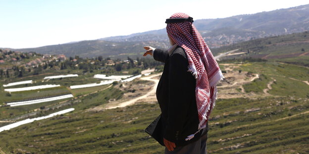 Ein Mann mit palästinensischer Kopfbedeckung zeigt in die Ferne.