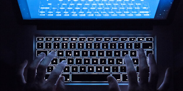 Auf der beleuchteten Tastatur eines Notebooks sind die Umrisse zweier Hände erkennbar