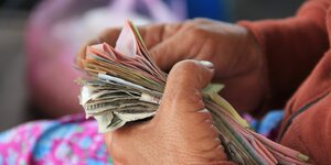 Die Hände einer älteren Frau halten ein Bündel Geldscheine