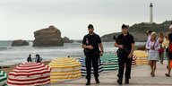Zwei bewaffnete Polizisten gehen am Strand von Biarritz entlang. Im Hintergrund befinden sich Badegäste