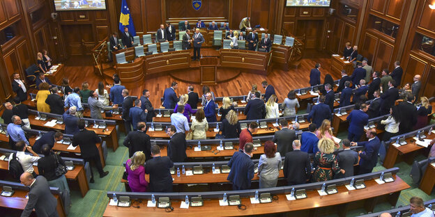 Abgeordnete sitzen und stehen im halbrunden Parlamentssaal