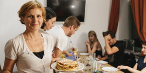 Katja Kipping steht vor einem Tisch, an dem Menschen sitzen, trägt einen Teller mit Eierkuchen