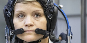 NASA-Astronautin Anne McClain blickt streng in die Kamera. Sie trägt ihre Astronautinnen-Ausrüstung, unter anderem enen Helm mit Mirkophonen.