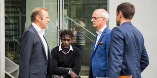 Bakery Jatta sitzt neben HSV-Chef Bernd Hoffmann auf dem DFB-Gelände auf einer Mauer.