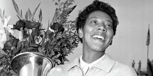 Althea Gibson hält Pokal mit Blumenstrauß darin. Es ist ein Schwarzweißbild