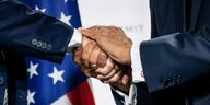 Das BIld zeigt eine Detailaufnahme von dem Moment, in dem sich Macron und Trump die Hand geben. Macrons linke Hand liegt obenauf. Im Hintergrund sieht man die US-amerikanische Flagge.
