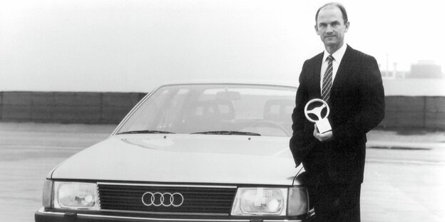 Ferdinand Piech im Jahr 1982 steht mit einem Goldenen Lenkrad in der Hand neben einem Audi 100 C3