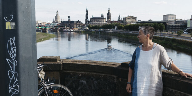 Eine Frau steht an einer Brüstung, im Hintergrund ein Fluss und eine Stadt, Dresden