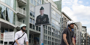 Männer rollern auf E-Scootern über den Checkpoint Charlie