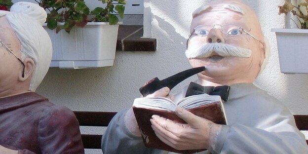 Skulptur eines alten Mannes mit Pfeife und Buch