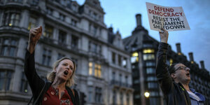Eine Frau und ein Mann demonstrieren mit erhobener Faust und Plakat gegen die Parlamentspause