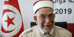 ein Mann mit Kopfbedeckung vor der tunesischen Flagge