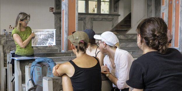 Ein Gruppe junger Menschen sitzt in einer Kirche und hört ihrer Wanderführerin zu