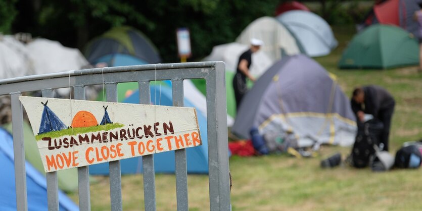 Zelte hinter einem Zaun mit einem Schild, auf dem steht "Zusammenrücken"