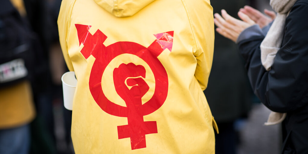 Beim Frauentag in Hamburg: Person mit gelbem Regenmantel, darauf ein Gender-Protest-Symbol in rot