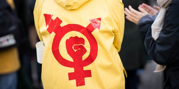 Beim Frauentag in Hamburg: Person mit gelbem Regenmantel, darauf ein Gender-Protest-Symbol in rot