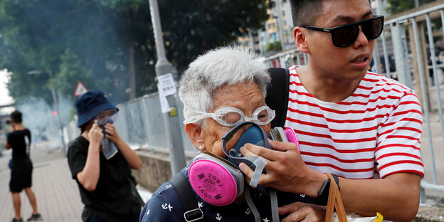 Ein junger Demonstrant hält einer älteren Dame eine Atemmaske aufs Gesicht, nachdem die Polizei bei den Protesten in Hongkong Tränengas eingesetzt hat. Die alte Frau trägt außerdem eine Schwimmbrille, um ihre Augen zu schützen
