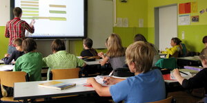 Schüler sitzen im Klassenraum vor einer digitalen Tafel