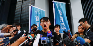 Ein Parteikollege von Joshua Wong, Isaac Cheng, steht vor einer Gruppe von Journalisten, die ihm Mikrofone entgegen halten