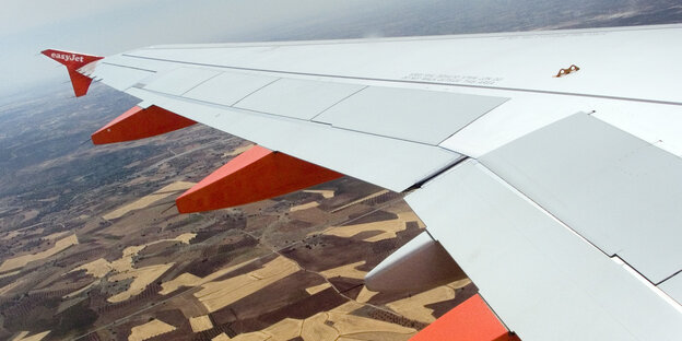 Die Tragfläche eines Flugzeugs aus dem Fenster fotografiert, darunter Feld