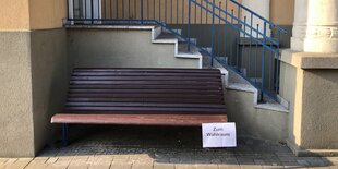 Eine braune Bank steht vor einer Treppe, an sie ist ein Zettel mit der Aufschrift „Zum Wahlraum“ geheftet