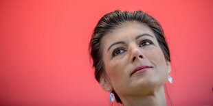 Sarah Wagenknecht vor rotem Hintergrund, sieht sehnsuchtsvoll nach oben