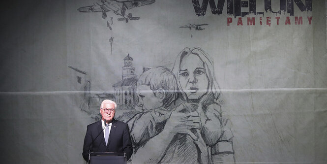 Frank-Walter Steinmeier hinter dem Redenerpult, im Hintergrund eine Zeichnung auf der Eien Frau mit Kind zu sehen ist, am Himmel ein Flugzeug mit Bomben.