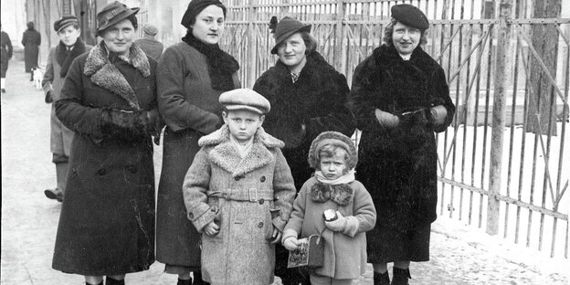 Das Schwarzweißfoto zeigt einen Jungen und ein Mädchen, hinter ihnen stehen vier Frauen, alle in winterlicher Kleidung.