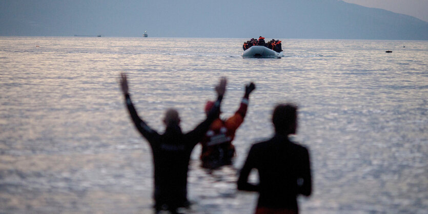 Im Boot ankommende Flüchtlinge werden von Helfern erwartet.