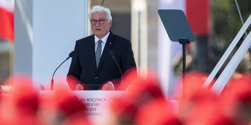 Steinmeier im Hintergrund am Redepult, unscharf im Vordergrund sind die roten Kappen der ZuhörerInnen