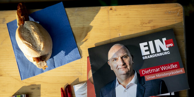 Wahlkampfflyer von Dietmar Woidke (SPD), Ministerpräsident von Brandenburg, und eine Bratwurst im Brötchen liegen bei der Wahlkampf-Abschlussveranstaltung der SPD