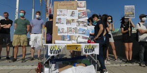 Demonstranten mit Mundschutz stehen neben einem Infostand