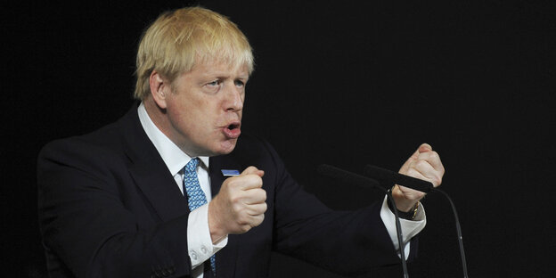 Boris Johnson steht an einem Rednerpult und ballt die Fäuste während er spricht.