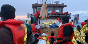 Menschen stehen mit Rettungswesten und -decken an Bord eines Schiffes