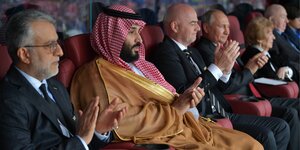 Der saudische Kronprinz Mohammed Bin Salman klatscht auf einer Tribüne Beifall, er trägt ein traditionelles saudisches Gewand. Neben ihm sitzt Vladimir Putin