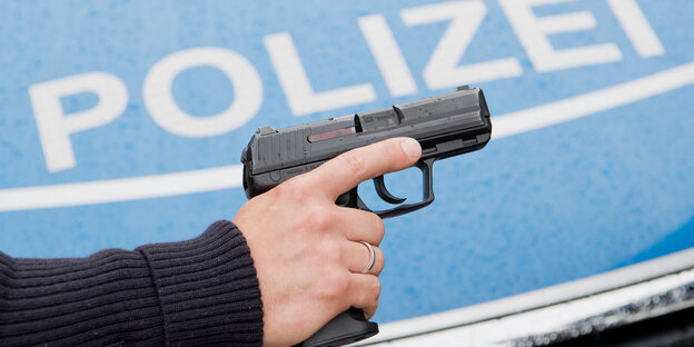 Ein Polizist zeigt seine Dienstwaffe HK P2000 9mm vor einem Polizeifahrzeug.