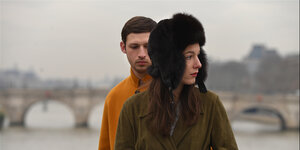 Das Standbild aus Nadav Lapids Film „Synonymes“ zeigt einen jungen Mann, der hinter einer jungen Frau steht. Der Himmel ist grau.