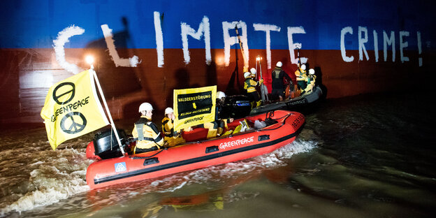Greenpeace-Leute in einem Schlauchboot bemalendie Wanad eines Frachters mit dem Schriftzug Climate Crime.