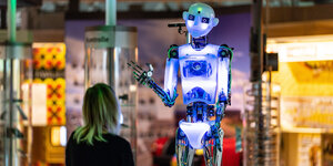 Eine Frau steht vor einem bläulich leuchtenden Roboter